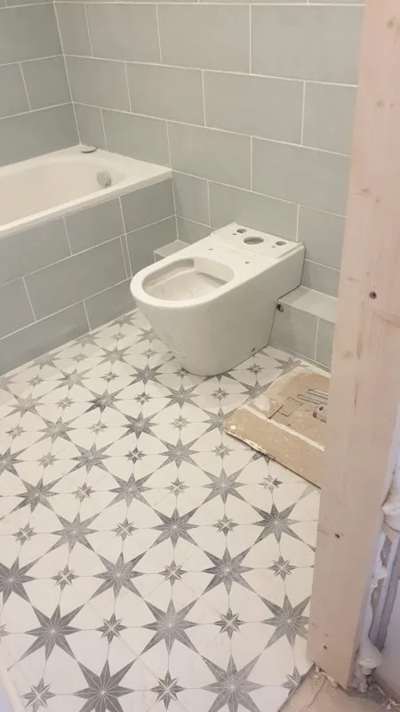 Bathroom with grey wall tiles, a bath and a patterned floor tile